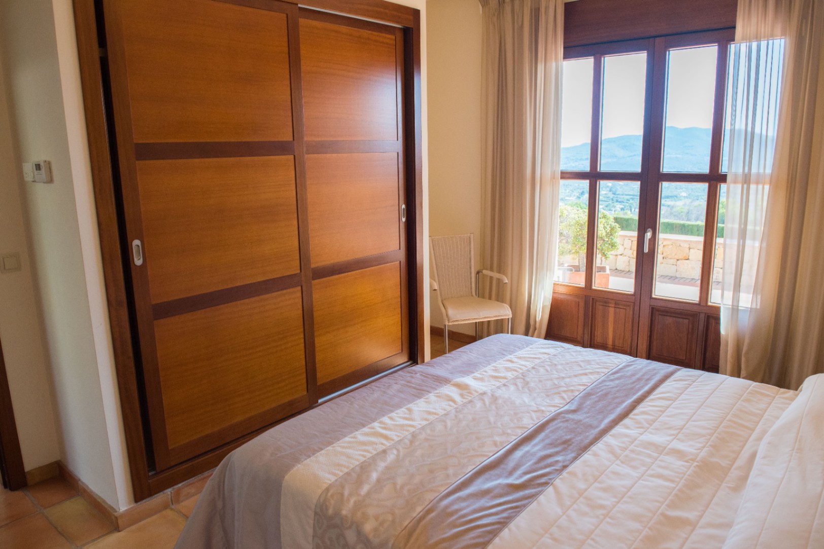 Schlafzimmer mit eingebautem Holzschrank, Schiebetüren und Zugang zu einer Terrasse mit weitem Blick auf die umliegenden Berge.