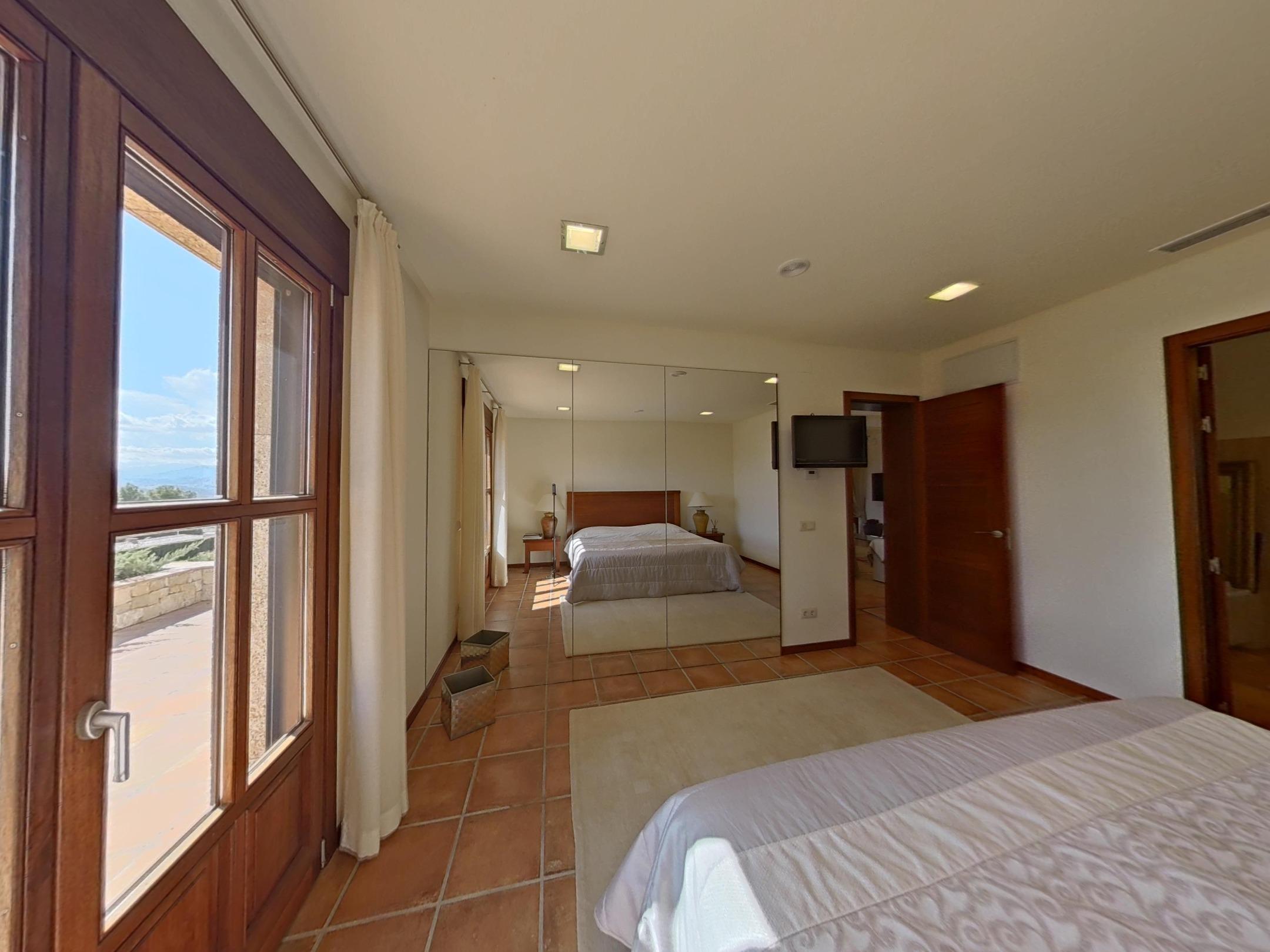 Schlafzimmer mit Terrakottaboden, raumhohen Spiegelschränken und Zugang zur Terrasse durch klassische Holzrahmentüren.