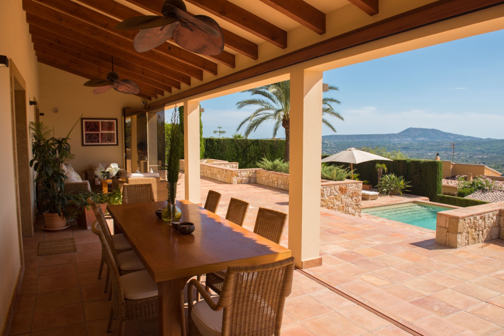 Überdachte Terrasse mit Holzbalkendecke, Terrakottaboden und Essbereich mit Blick auf den privaten Pool und die umliegende Berglandschaft.