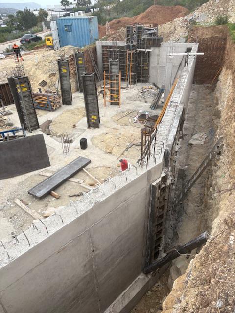 Fundamentphase mit Stützwänden aus Stahlbeton und vertikalen Schalungen für tragende Säulen auf einer vorbereiteten Baustelle.