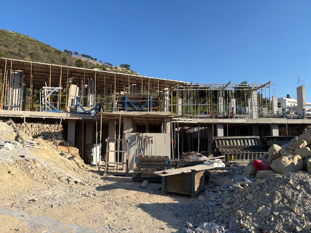 Rohbau einer modernen Villa mit Stahlbetonstützen, Metallstützen und Holzschalungen in Hanglage unter klarem blauem Himmel.