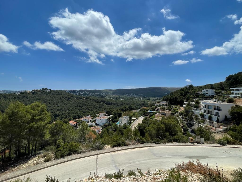 Erhöhter Panoramablick auf ein mediterranes Tal mit weißen Villen zwischen pinienbewachsenen Hügeln unter einem strahlend blauen Wolkenhimmel.