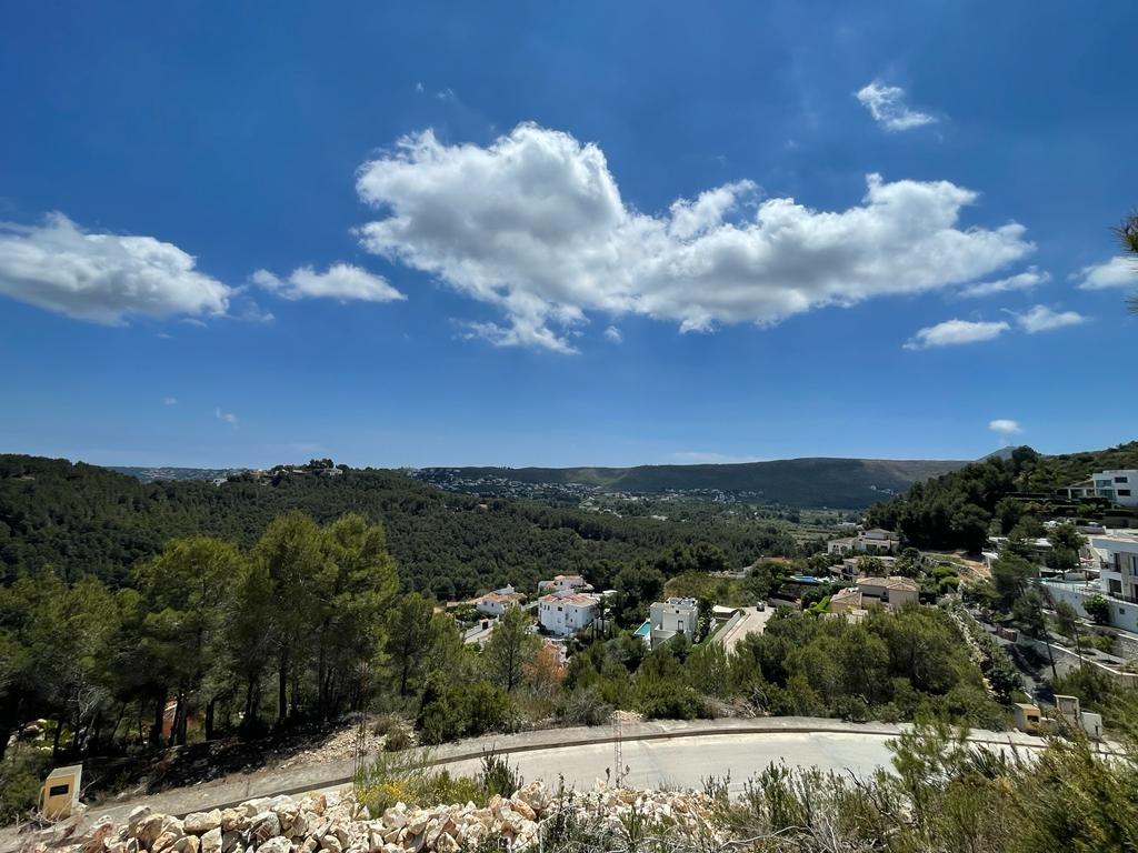 Erhöhter Panoramablick über ein grünes Kieferntal mit weißen Villen, sanften Hügeln und klarem blauem Himmel mit Wolken.