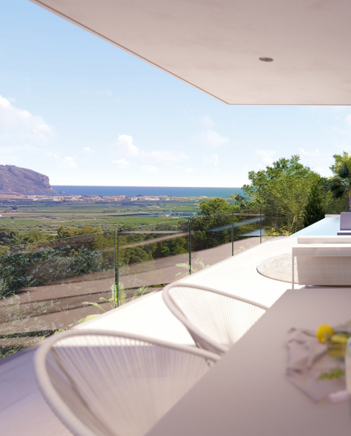 Erhöhte Terrasse mit Glasbalustrade und Panoramablick auf das Mittelmeer und die Berge. Ausgestattet mit modernen weißen Kordelstühlen und hellem Fliesenboden.