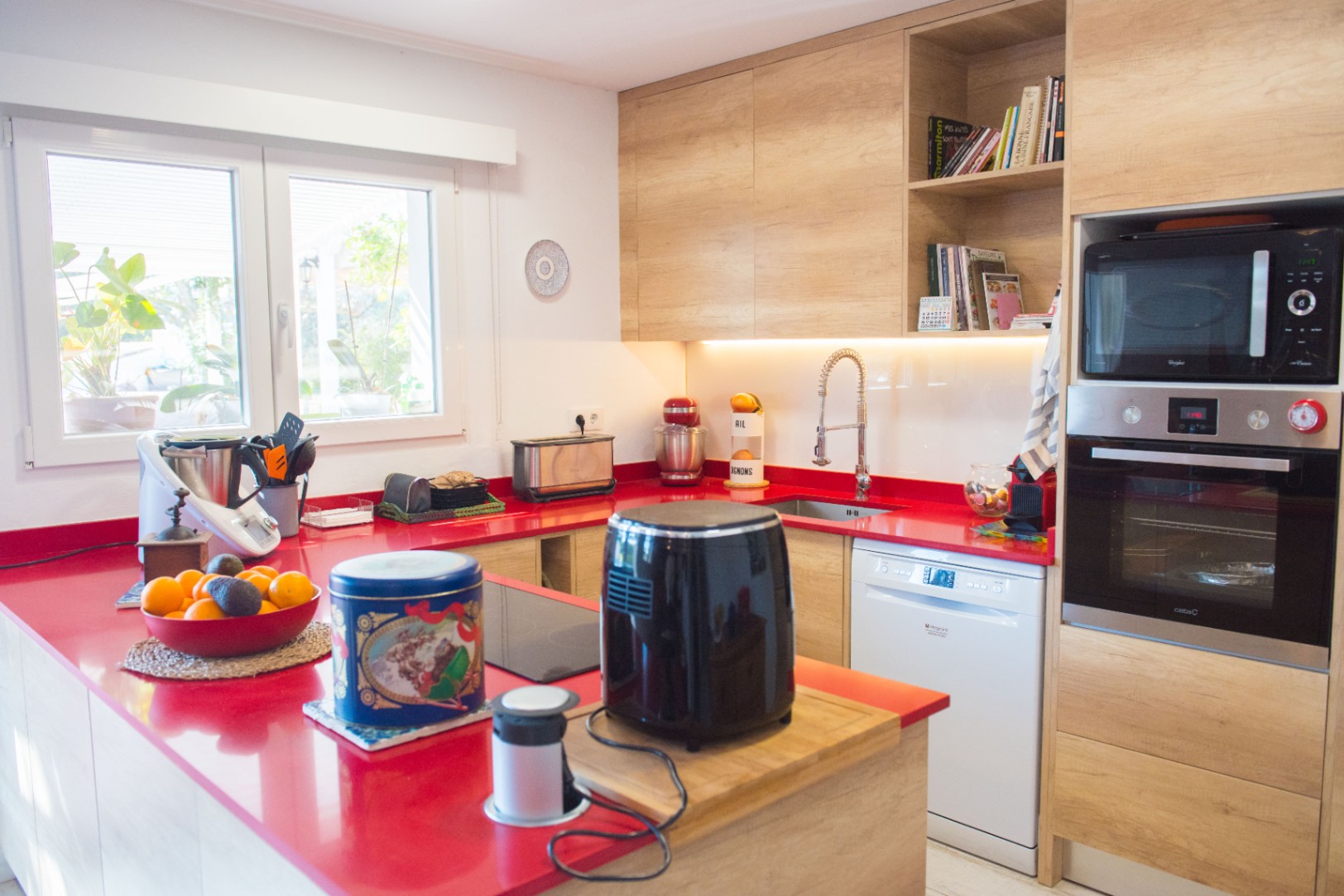 Moderne Küche mit markanter roter Arbeitsplatte, hellen Holzschränken und integrierten Geräten wie Backofen, Mikrowelle und Geschirrspüler.