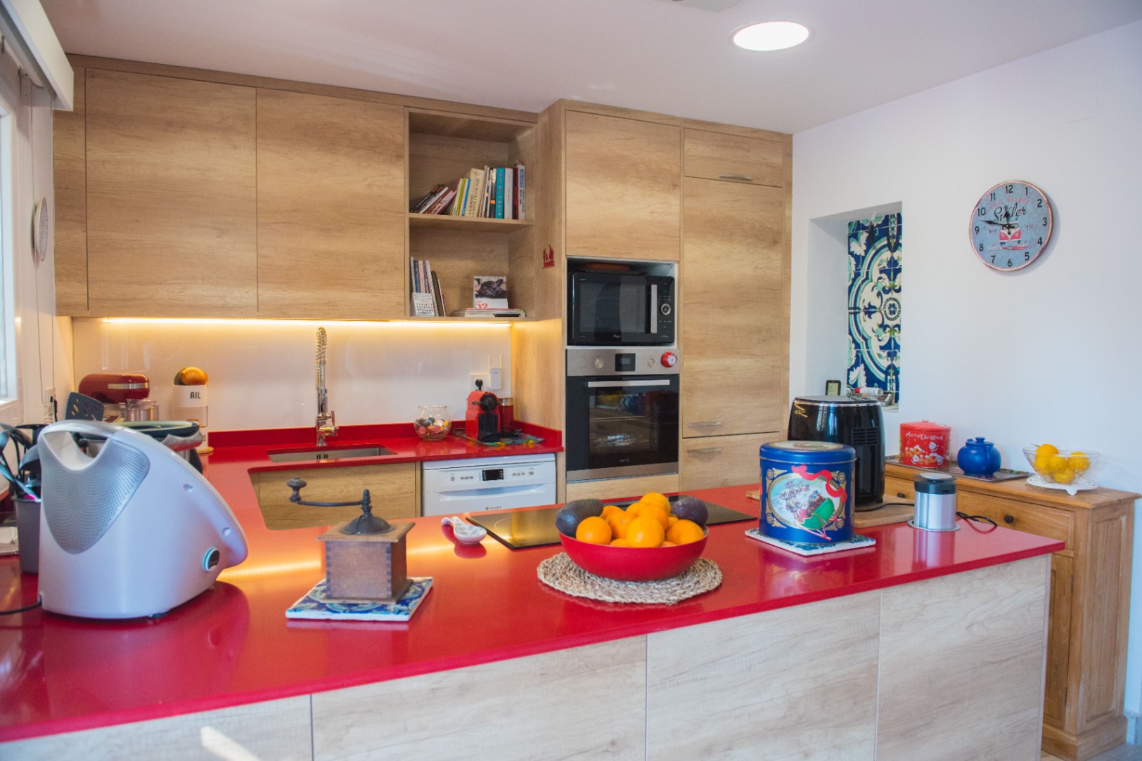 Moderne Küche mit markanter roter Arbeitsplatte, hellen Holzschränken und integrierten Geräten wie Backofen und Induktionskochfeld.