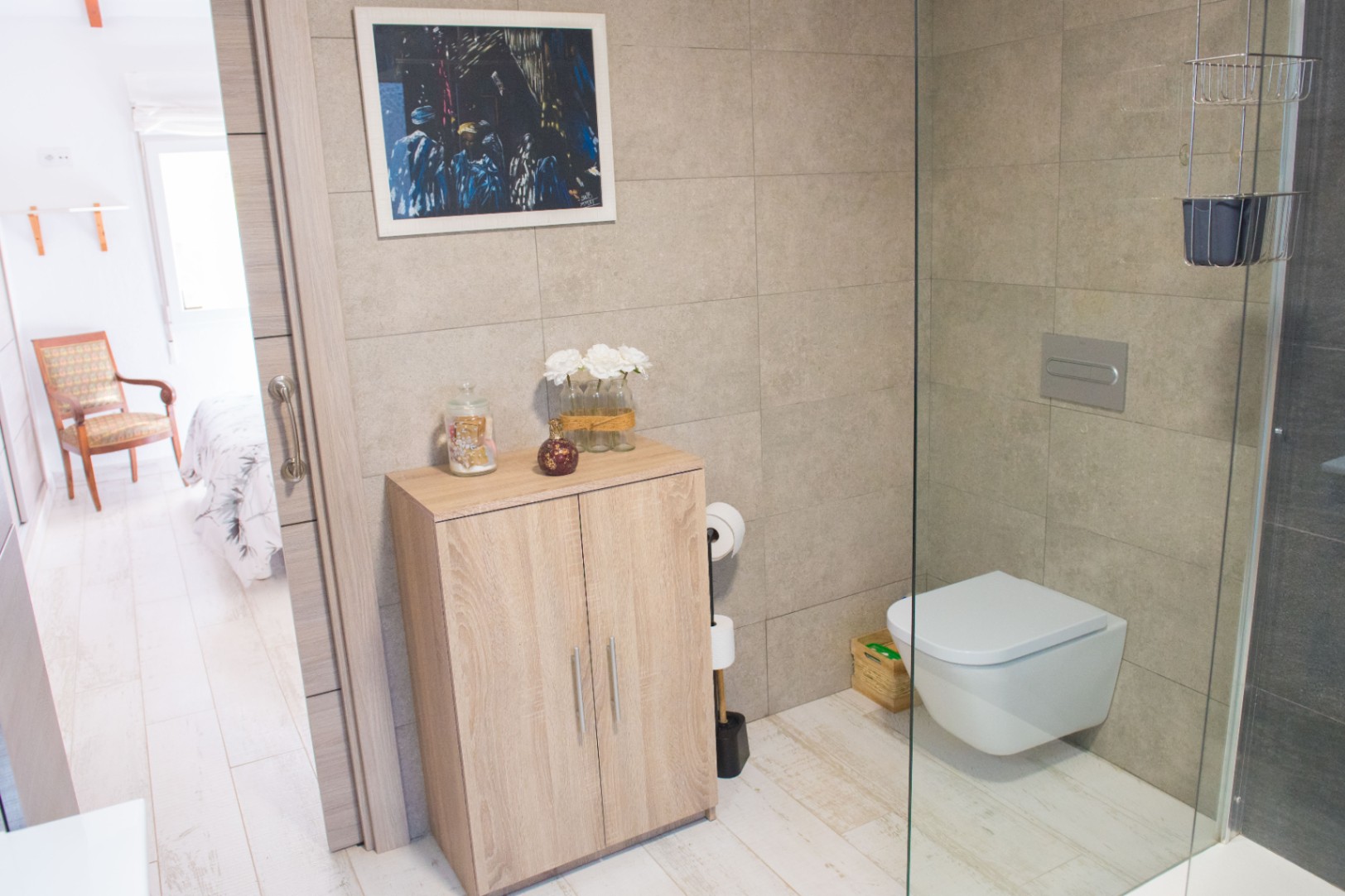 Modernes Badezimmer mit wandhängendem WC, Glasduschwand und hellem Holzschrank vor großformatigen beigen Wandfliesen.