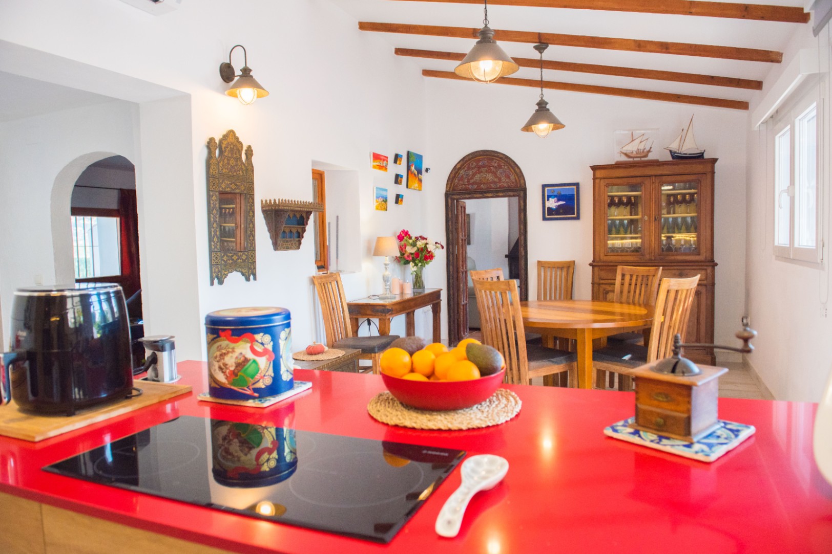 Offene Küche mit markanter roter Arbeitsplatte und Induktionskochfeld, angrenzend an einen Essbereich mit sichtbaren Deckenbalken und rustikalen Massivholzmöbeln.