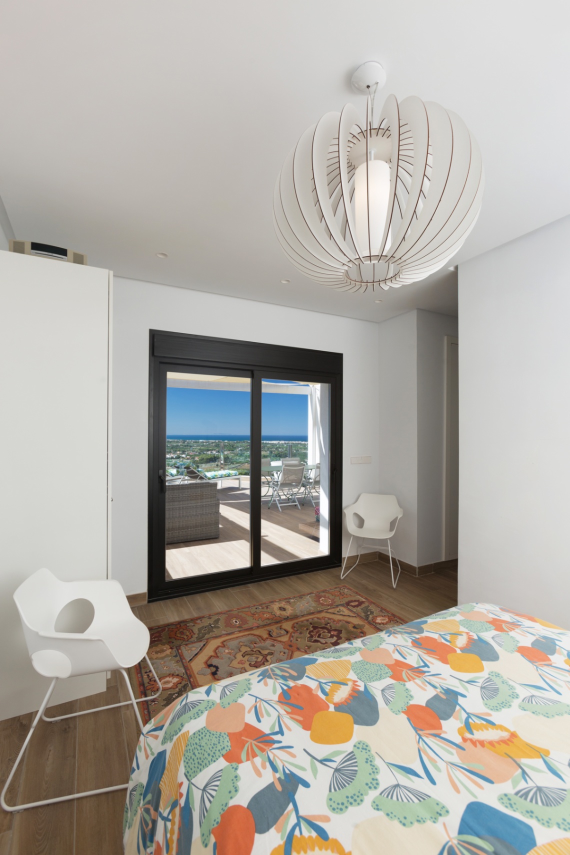 Helles Schlafzimmer mit direktem Terrassenzugang durch schwarze Schiebetüren, Design-Pendelleuchte und Panoramablick auf das Meer.