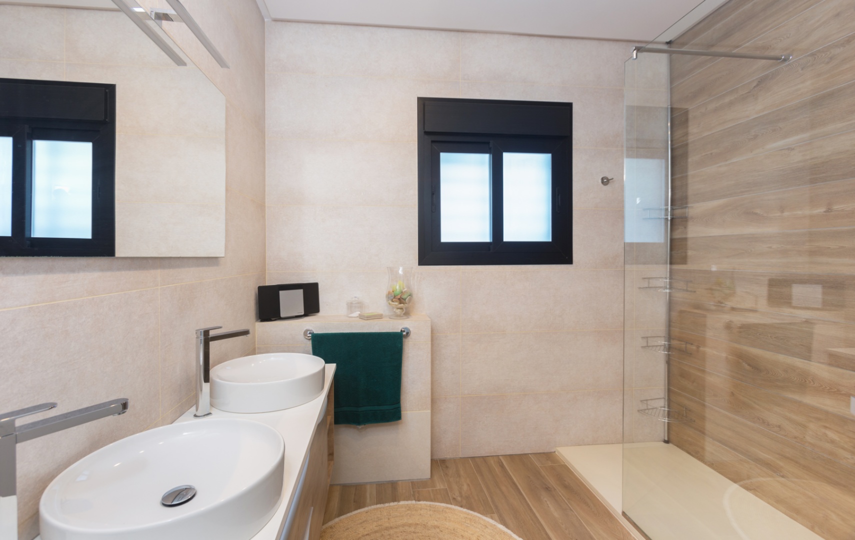 Modernes Badezimmer mit Doppelwaschbecken, Fliesen in Holzoptik am Boden und in der Dusche sowie einer Glastrennwand und einem Fenster mit schwarzem Rahmen.