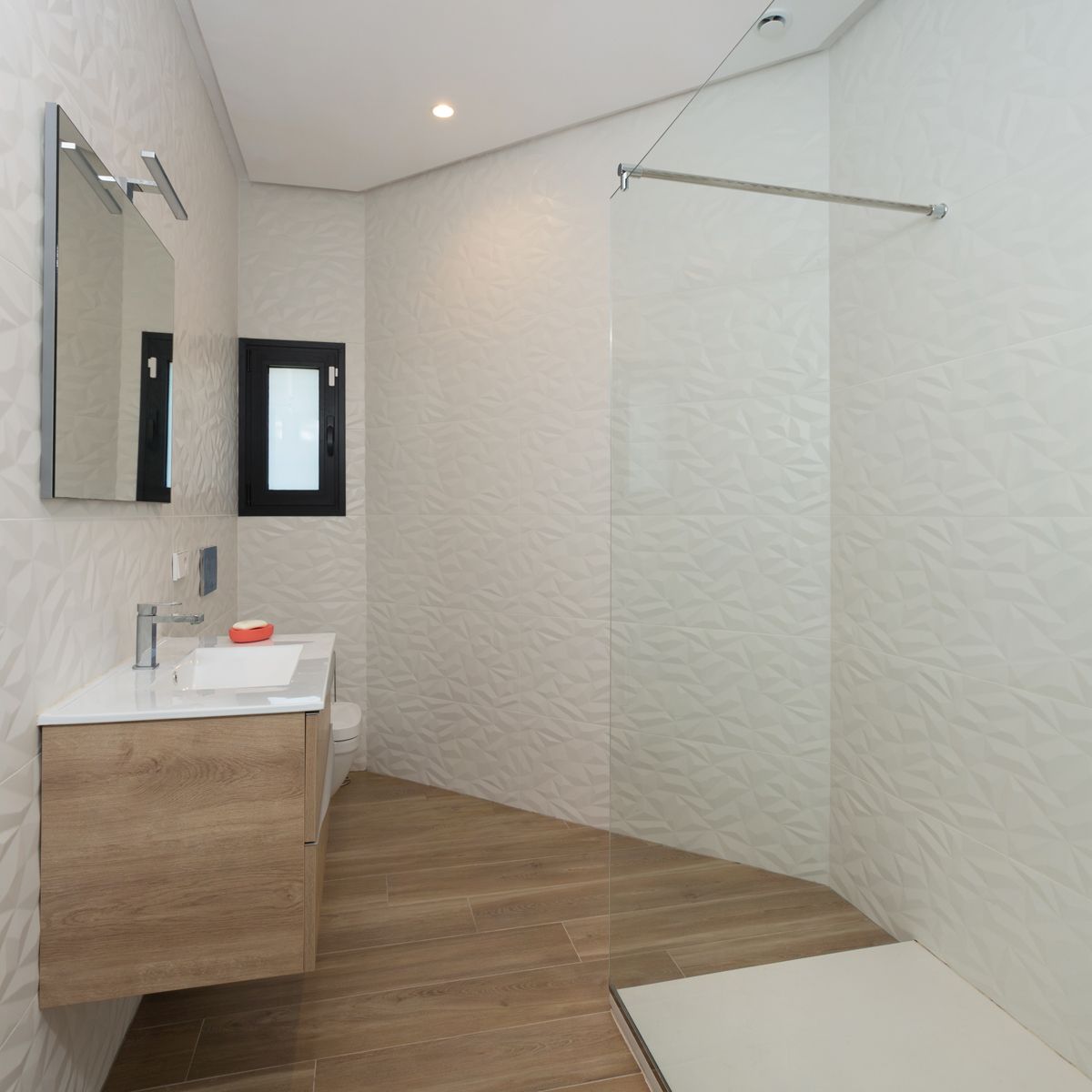 Modernes Badezimmer mit geometrisch strukturierten Wandfliesen, schwebendem Holzwaschtisch und bodengleicher Dusche mit Glastrennwand.