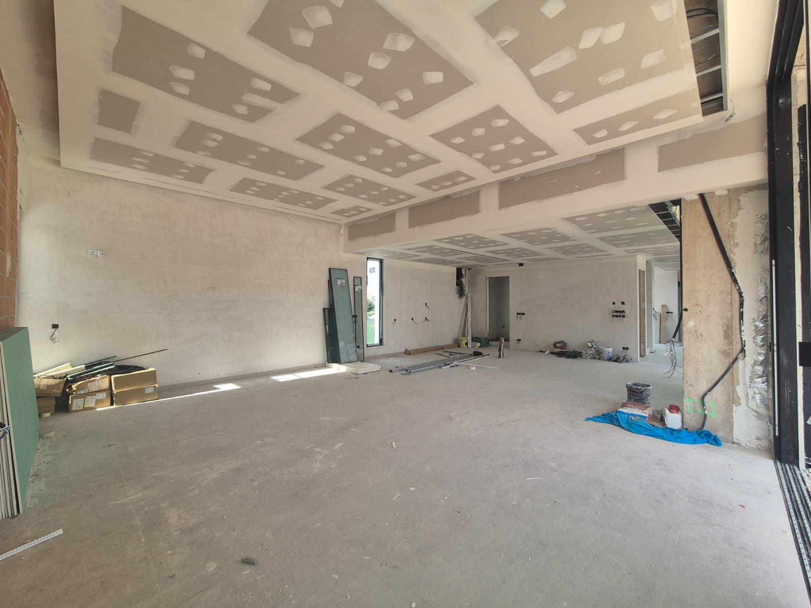 Großzügiger Innenraum im Rohbau mit mehrstufigen Gipskartondecken für indirekte Beleuchtung und bodentiefen Fensteröffnungen.