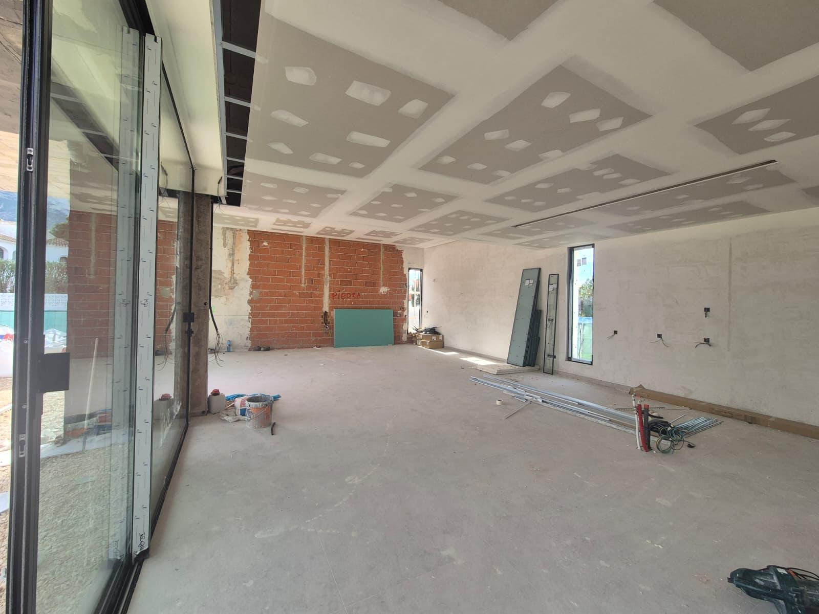 Großzügiger Wohnbereich im Rohbau mit Gipskartondecke für Einbaustrahler, Sichtmauerwerk und bodentiefen Glasschiebetüren.