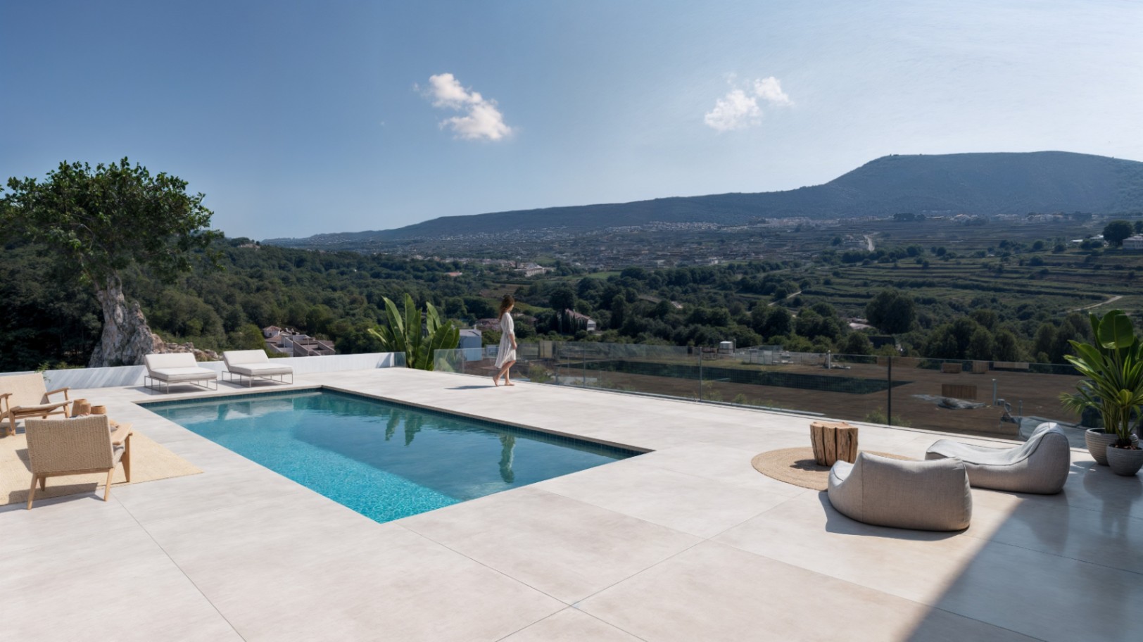 Erhöhte Terrasse mit rechteckigem Pool, großformatigen Steinplatten und Glasgeländer mit Panoramablick auf das grüne Tal und die umliegenden Berge.