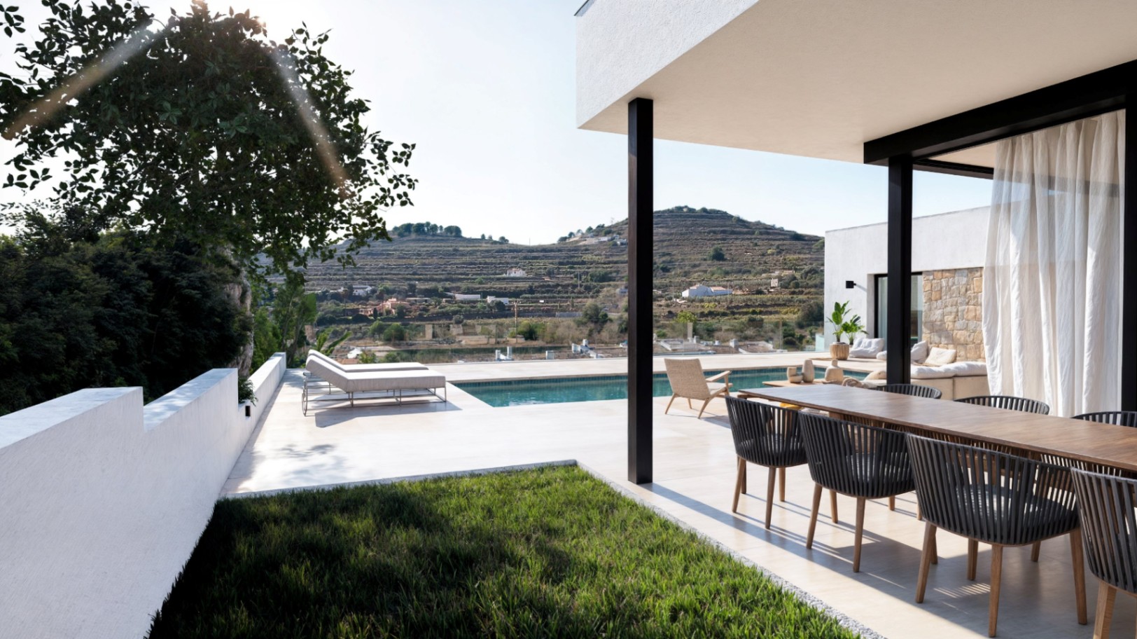 Moderne Außenterrasse mit Essbereich aus Holz, Pool und Sonnenliegen, mit Blick auf eine terrassierte Hügellandschaft und das umliegende Tal.