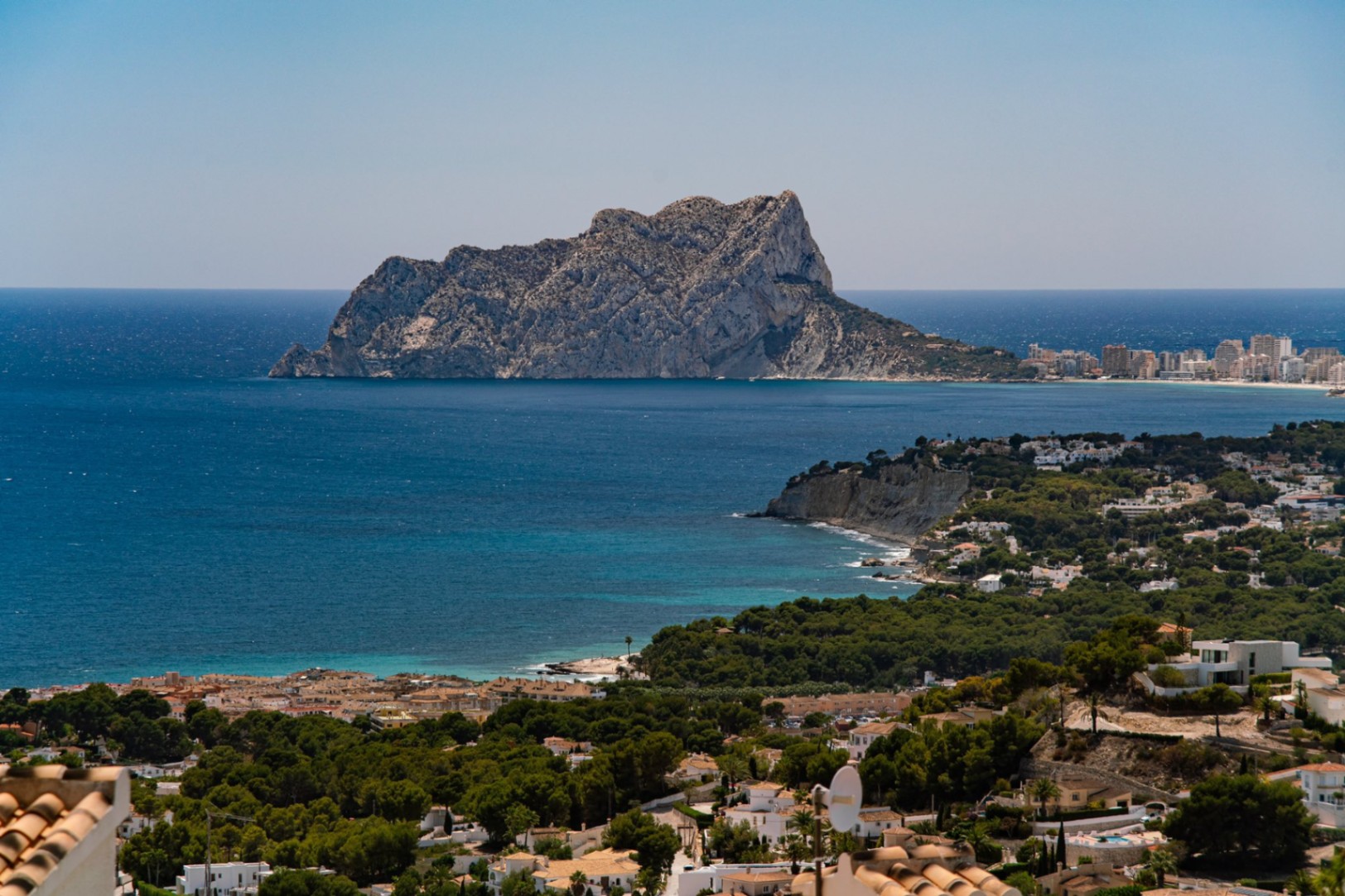 Erhöhter Panoramablick auf die Mittelmeerküste mit dem Peñón de Ifach, türkisblauem Wasser und einem in dichte Pinienwälder eingebetteten Wohngebiet.