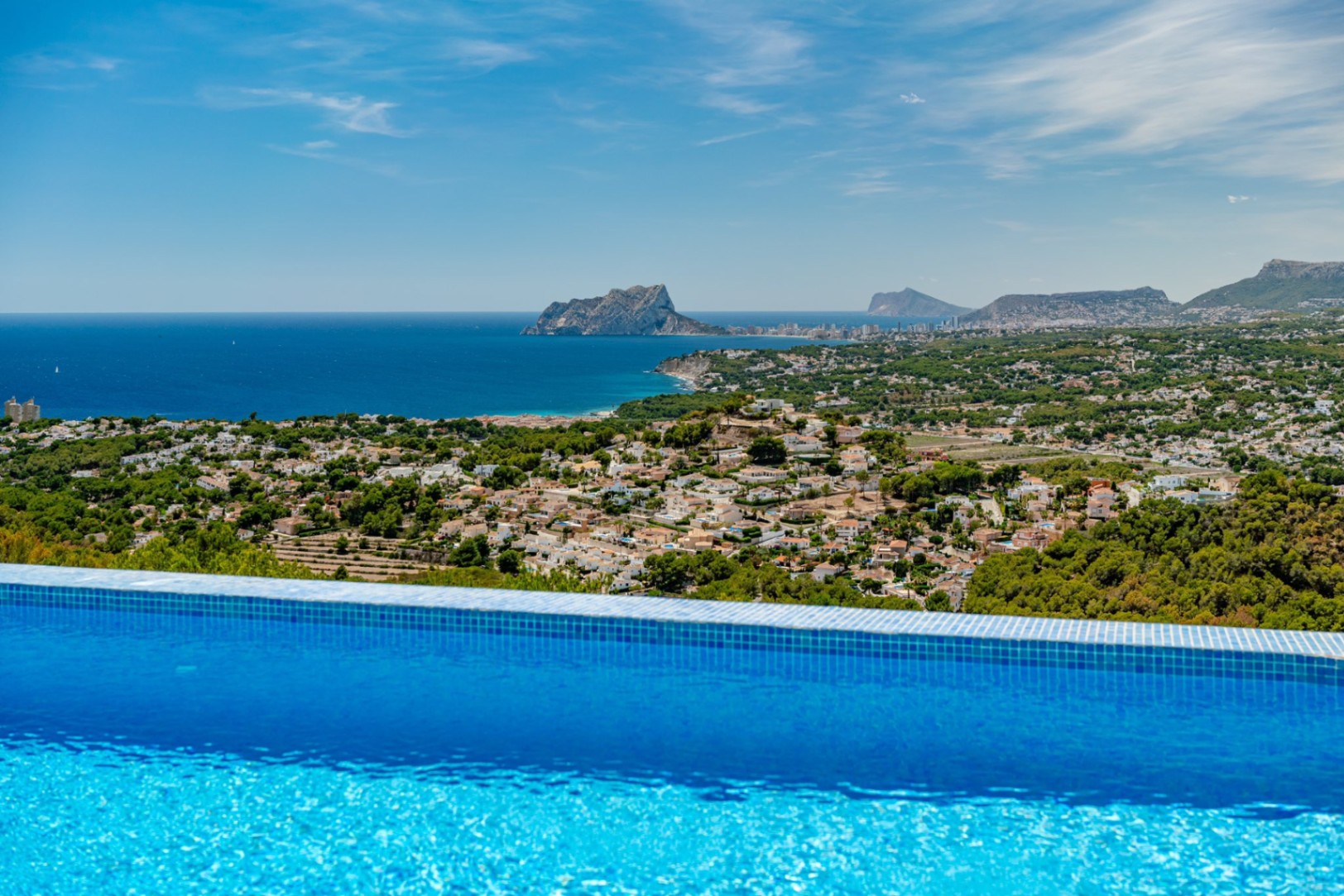 Infinity-Pool mit blauen Mosaikfliesen und Panoramablick auf das Mittelmeer, den Peñón de Ifach und die Küstenlandschaft von Calpe.
