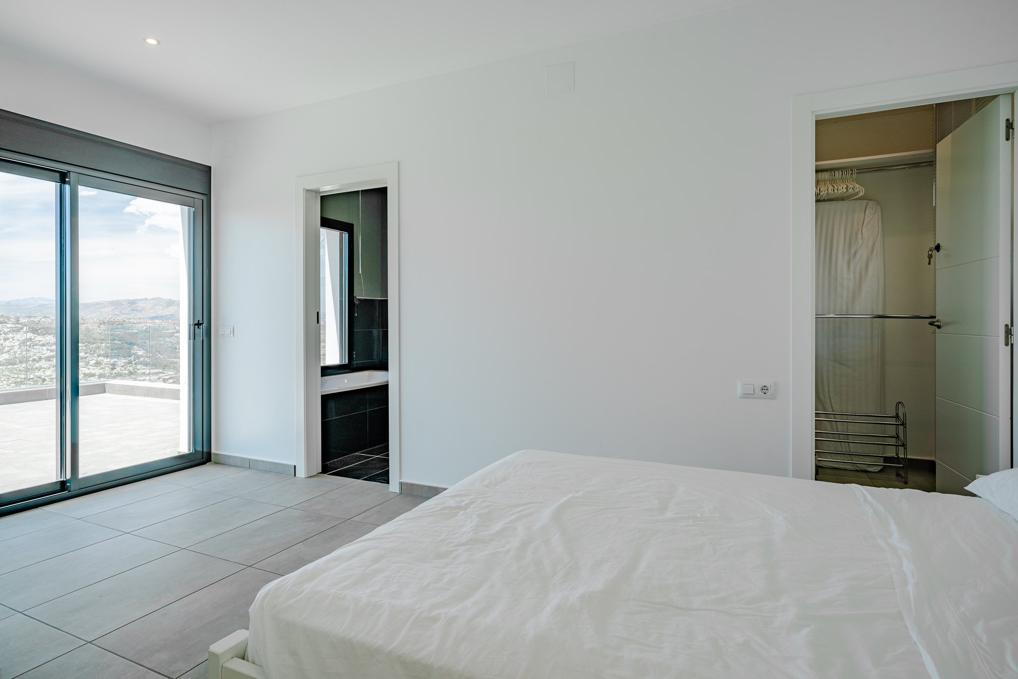 Modernes Schlafzimmer mit Glasschiebetür zur Terrasse, en-suite Badezimmer mit dunklen Fliesen und einem begehbaren Kleiderschrank.