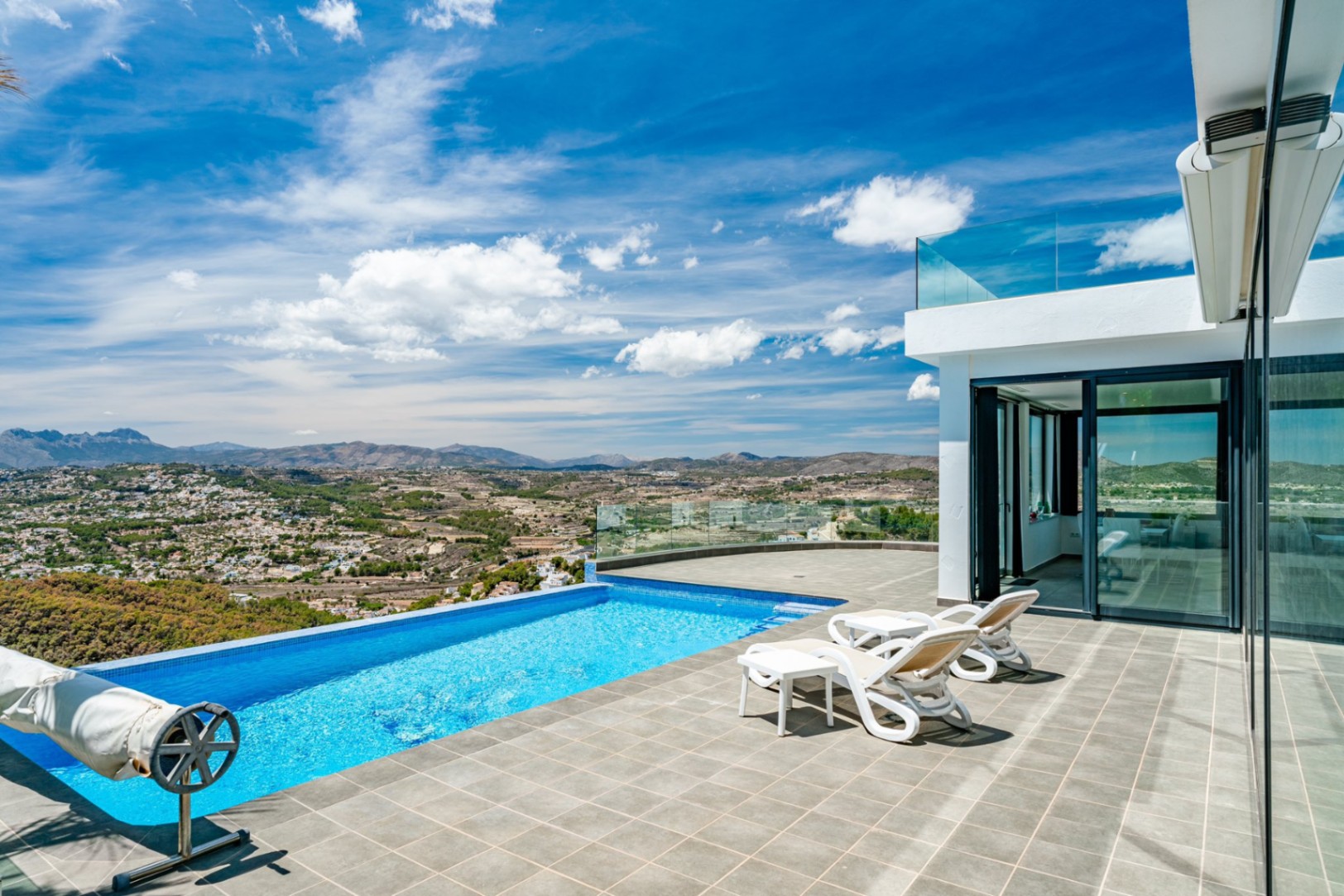 Terrasse mit Infinity-Pool und Glasgeländern mit Panoramablick auf das Tal. Ausgestattet mit Steinfliesen, Sonnenliegen und moderner weißer Architektur.