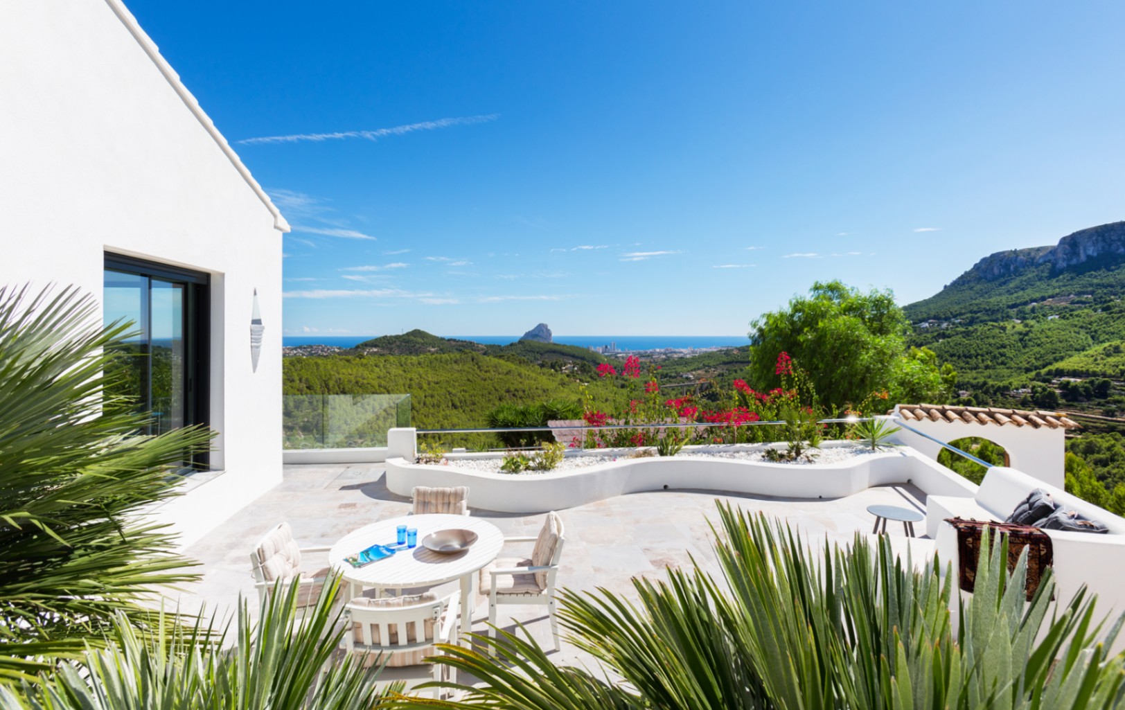 Großzügige, steinbelegte Terrasse mit Essbereich und geschwungenen Pflanzgefäßen, die einen Panoramablick auf die Mittelmeerküste und den Peñón de Ifach bietet.