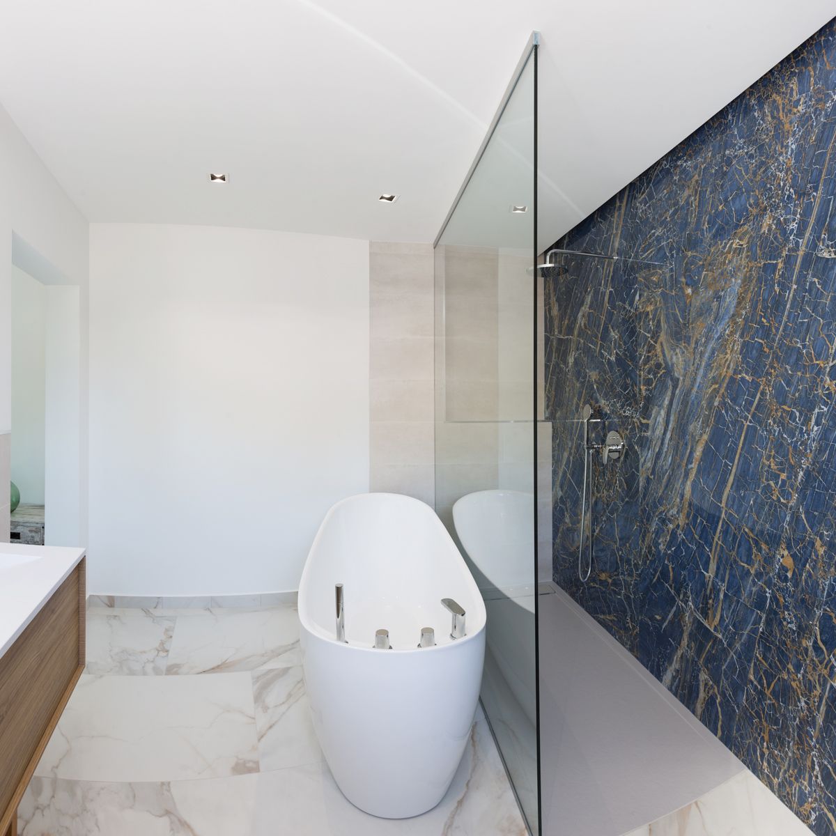 Modernes Badezimmer mit freistehender ovaler Badewanne, begehbarer Dusche mit blauer Marmorwand und weißem Marmorboden mit Goldmaserung.