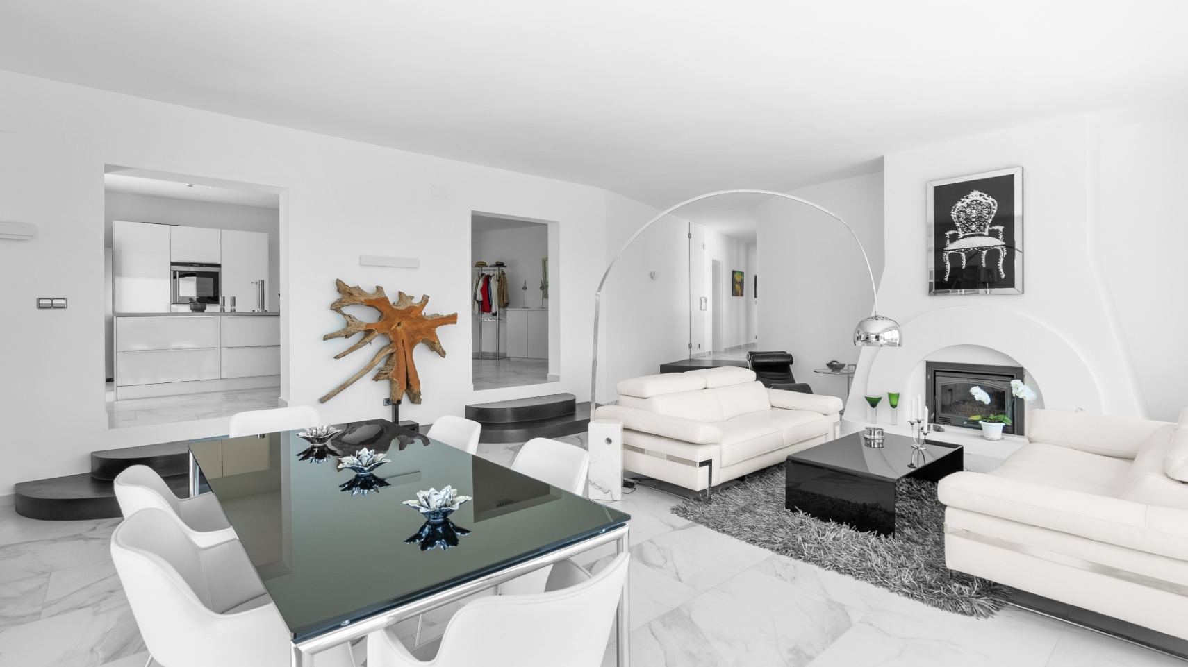Offener Wohn- und Essbereich mit Marmorboden, weißen Ledersofas, modernem Kamin und Glastisch, mit Blickachsen in die minimalistische Küche.
