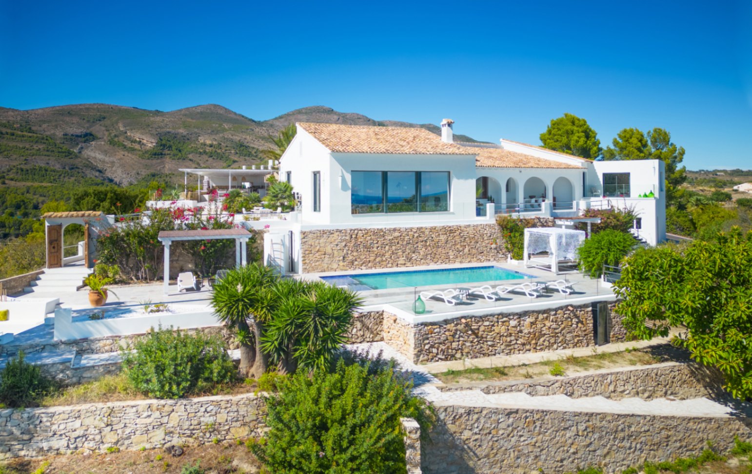Weiße mediterrane Villa mit Pool, Trockensteinmauern und Terrakottadach, eingebettet in eine weitläufige Berglandschaft.