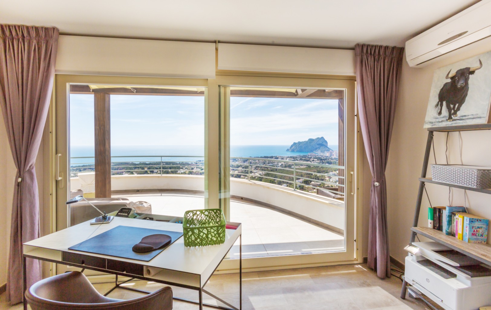 Arbeitszimmer mit modernem Schreibtisch und Regalen, inklusive großer Glasschiebetüren zur Terrasse mit weitem Blick auf das Meer und den Peñón de Ifach.