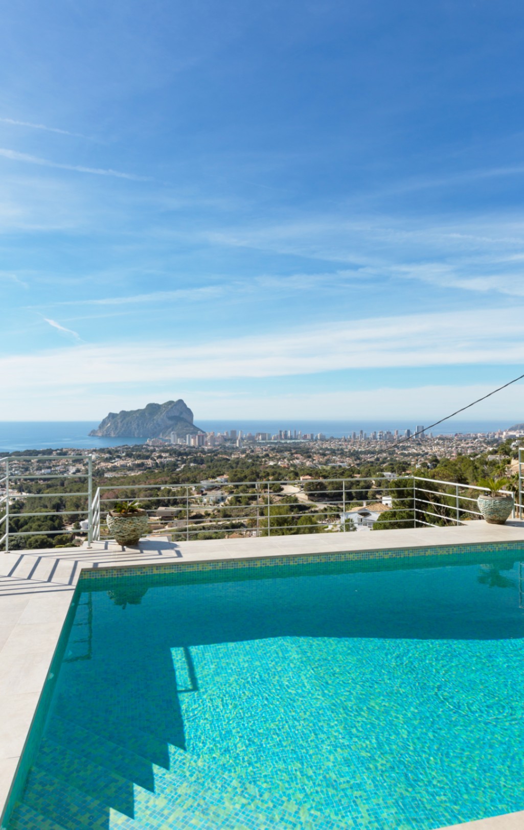 Erhöhte Terrasse mit türkisfarbenem Mosaikpool und weißer Steinumrandung, die einen Panoramablick auf den Peñón de Ifach und die Mittelmeerküste bietet.
