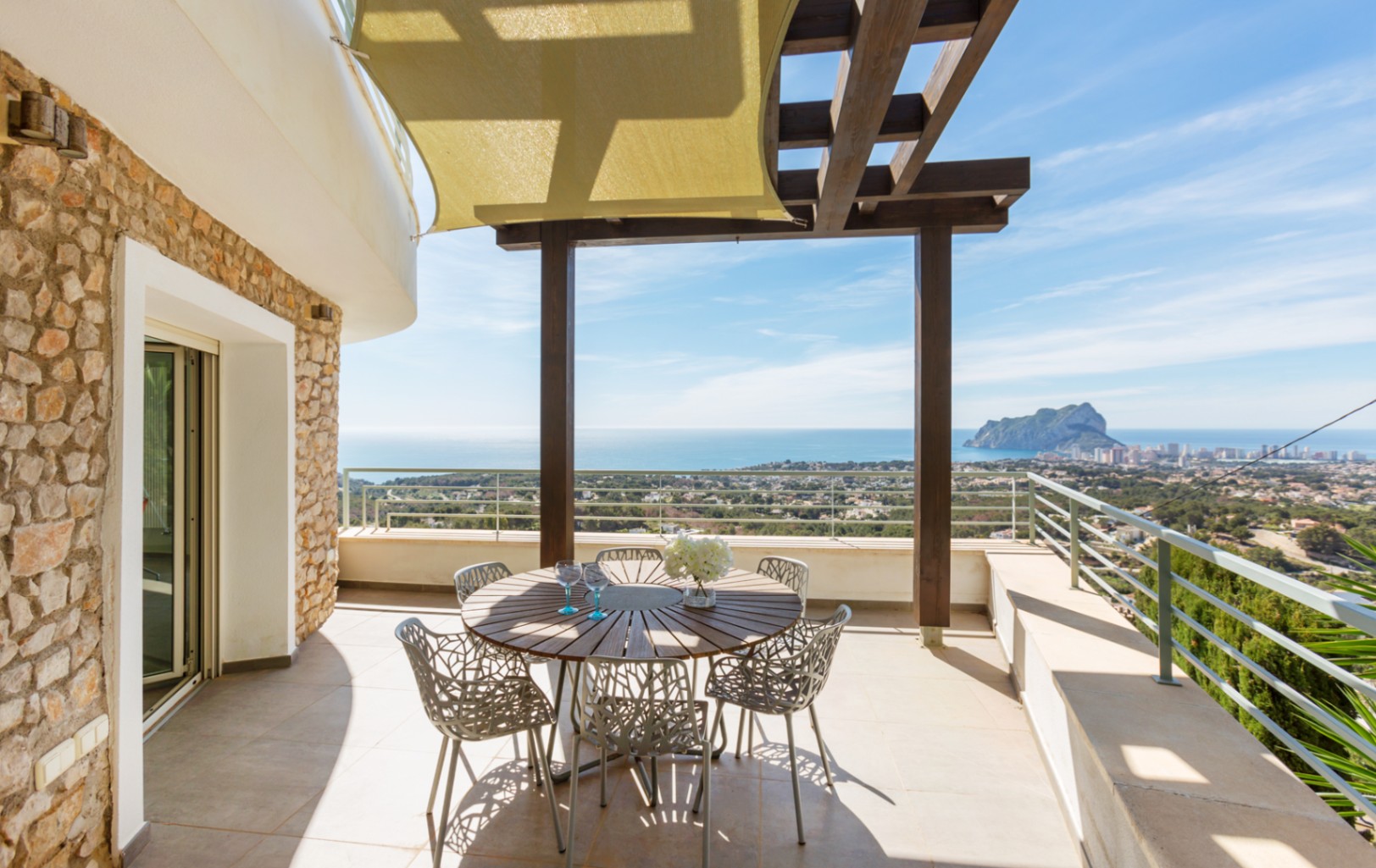 Terrasse mit Natursteinwänden, Holzpergola und Sonnensegel. Essbereich im Freien mit Panoramablick auf das Mittelmeer und den Peñón de Ifach.
