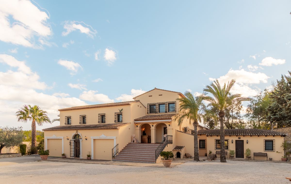 Außenansicht einer mediterranen Villa mit cremefarbener Fassade, Terrakottadach, breiter Treppe zum Rundbogenportal und integrierten Garagen.