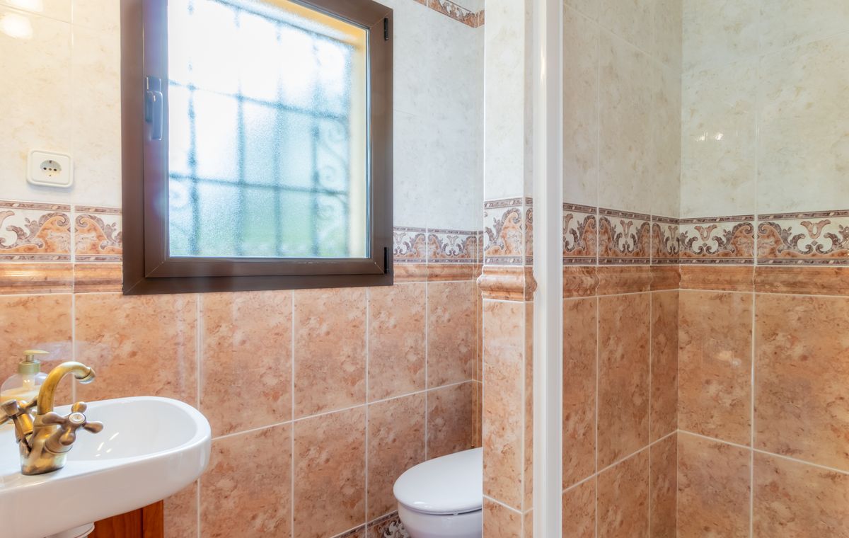 Badezimmer mit marmorierten Fliesen in Terrakotta-Tönen, einer klassischen Messingarmatur am Waschbecken und einem blickdichten Fenster mit Gitter.