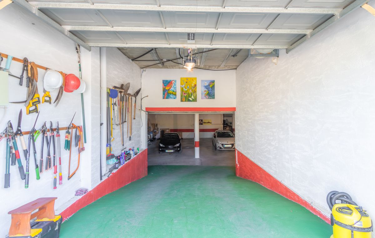 Geräumige Garage mit grüner Rampe, organisierter Werkzeugwand an weißen Wänden und einer unteren Ebene mit Parkplätzen für mehrere Fahrzeuge.