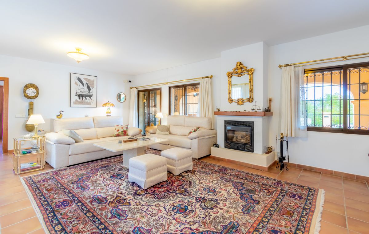 Großzügiges Wohnzimmer mit Terrakottaboden, Kamin mit prunkvollem Goldspiegel und weißen Sofas auf einem großen, gemusterten Teppich.