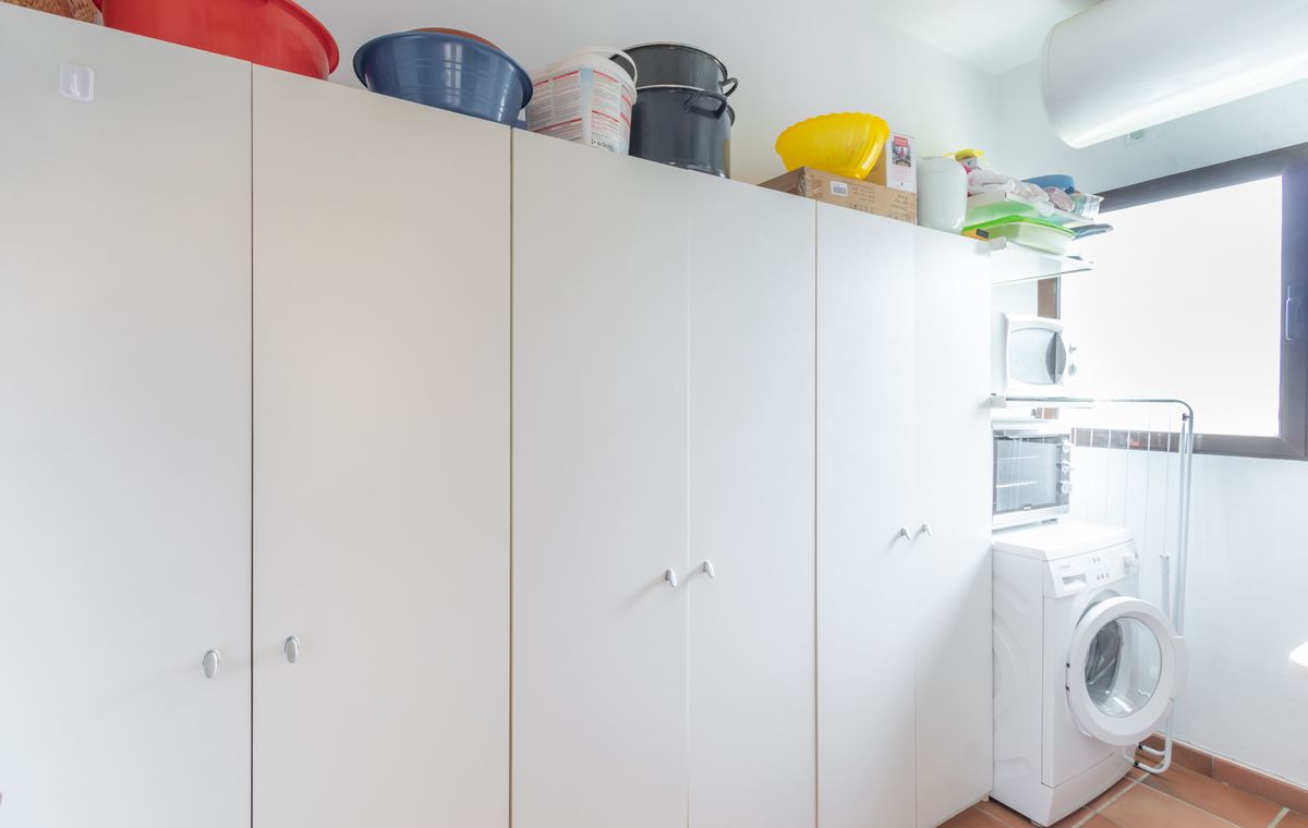 Hauswirtschaftsraum mit großzügigen weißen Schränken, Terrakottaboden und einem Waschbereich mit Waschmaschine und Mikrowelle.