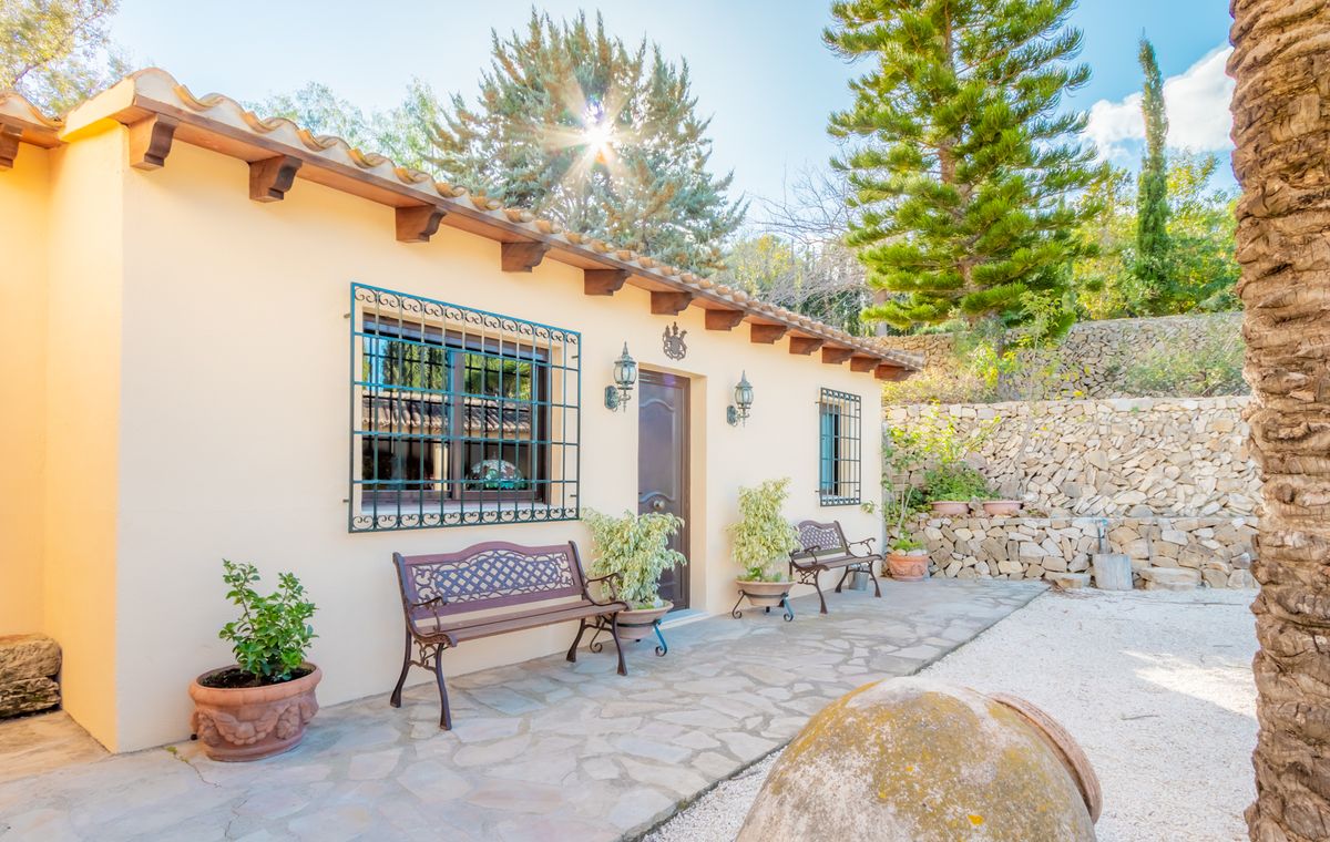 Mediterrane Fassade mit sichtbaren Holzbalken, schmiedeeisernen Fenstergittern und einer Natursteinterrasse mit dekorativen Bänken.