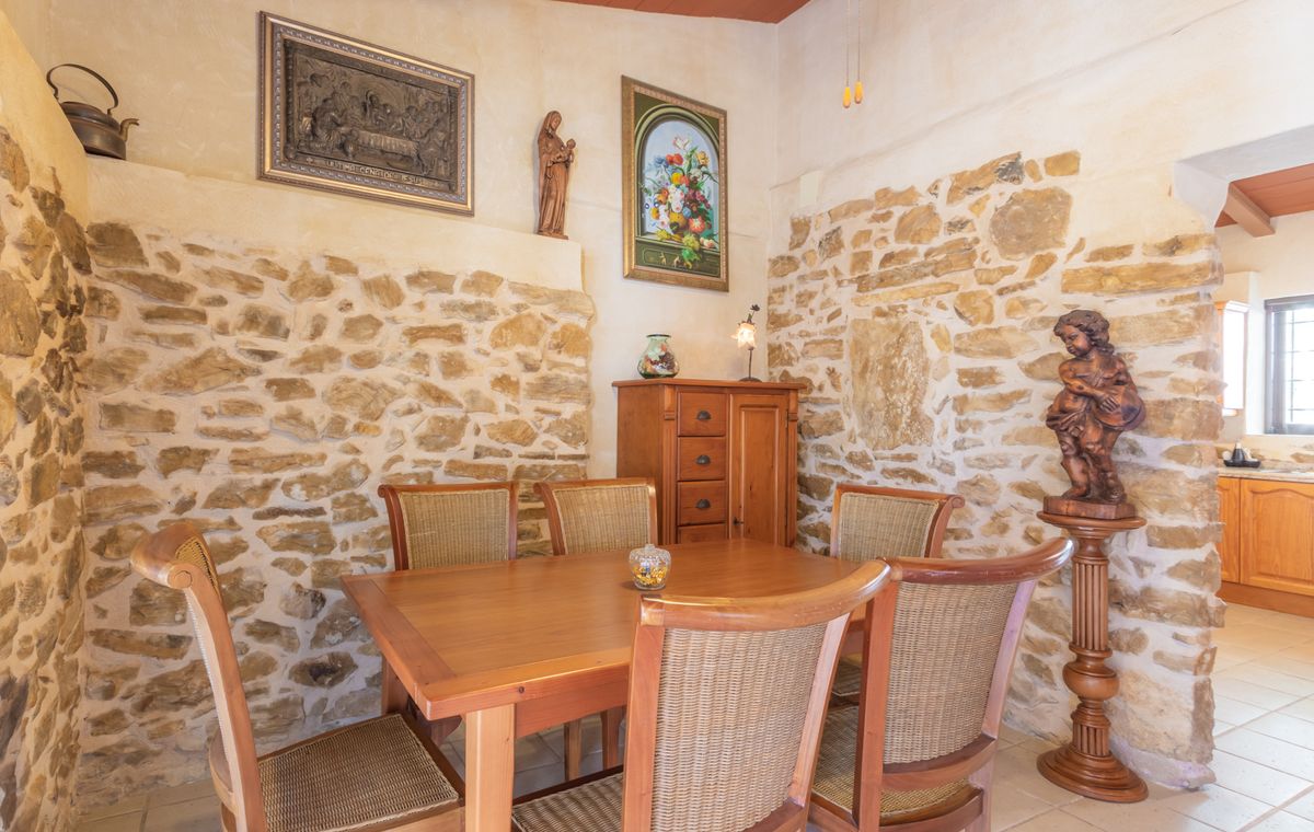 Rustikaler Essbereich mit freigelegten Natursteinwänden, Massivholztisch mit Korbstühlen und traditionellen religiösen Kunstwerken und Skulpturen.
