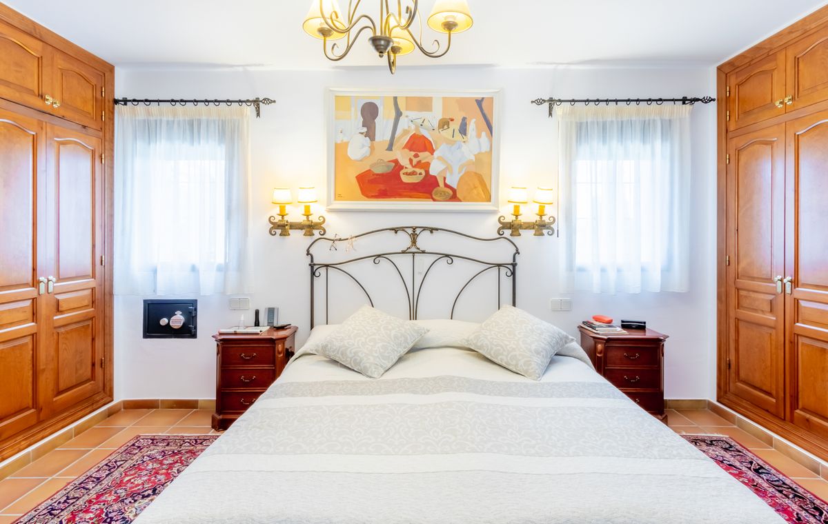Schlafzimmer mit schmiedeeisernem Kopfteil, symmetrischen Einbauschränken aus Holz und Terrakottaboden. Mit Wandleuchten und einem eingebauten Safe.