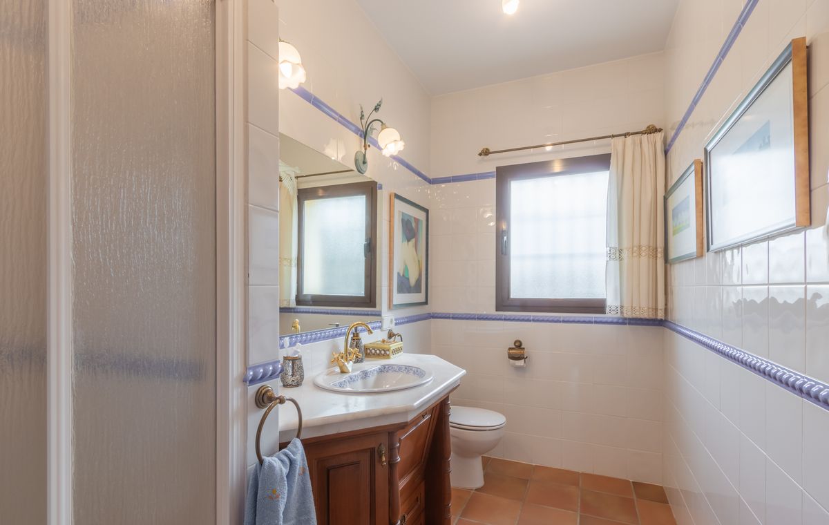 Traditionelles Badezimmer mit weißen Wandfliesen, blauen Zierleisten, einem Holzwaschtisch mit Marmorplatte und Terrakotta-Boden.