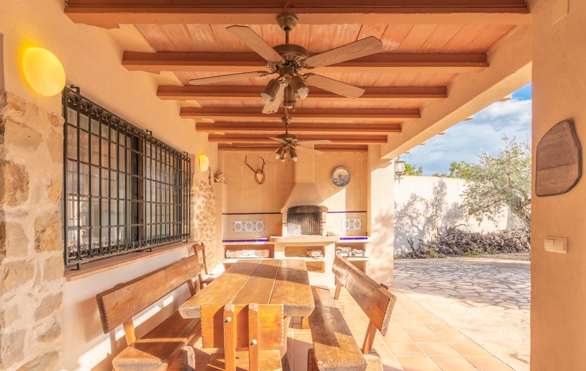 Überdachte Terrasse mit Holzbalkendecke, Deckenventilatoren, rustikaler Sitzgruppe und gemauertem Grill mit dekorativen Fliesen und Steinwänden.