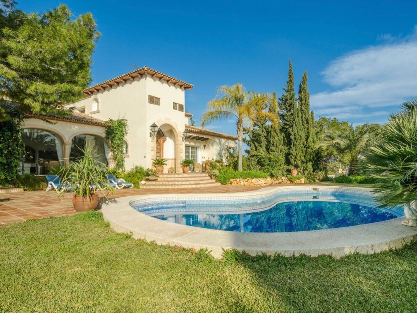 Mediterrane Villa mit geschwungenem Pool, Terrakotta-Terrasse und weißer Putzfassade mit traditionellen Rundbögen und gepflegtem, altem Baumbestand.