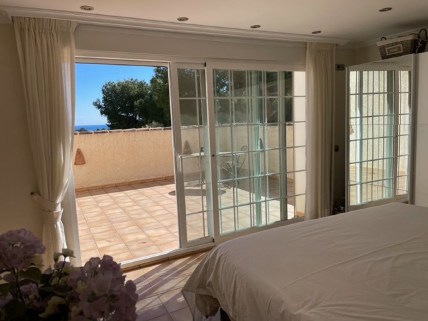 Schlafzimmer mit großen Glasschiebetüren, die auf eine private geflieste Terrasse mit Meerblick und Außenmöbeln führen.