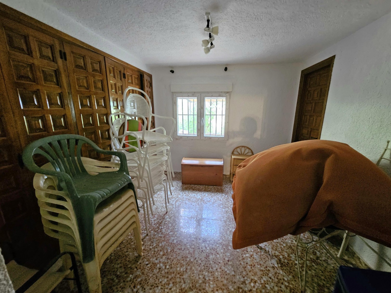 Raum mit eingebauten Holzschränken, Terrazzoboden und einem vergitterten Fenster. Funktionaler Bereich mit viel Stauraum und natürlichem Licht.