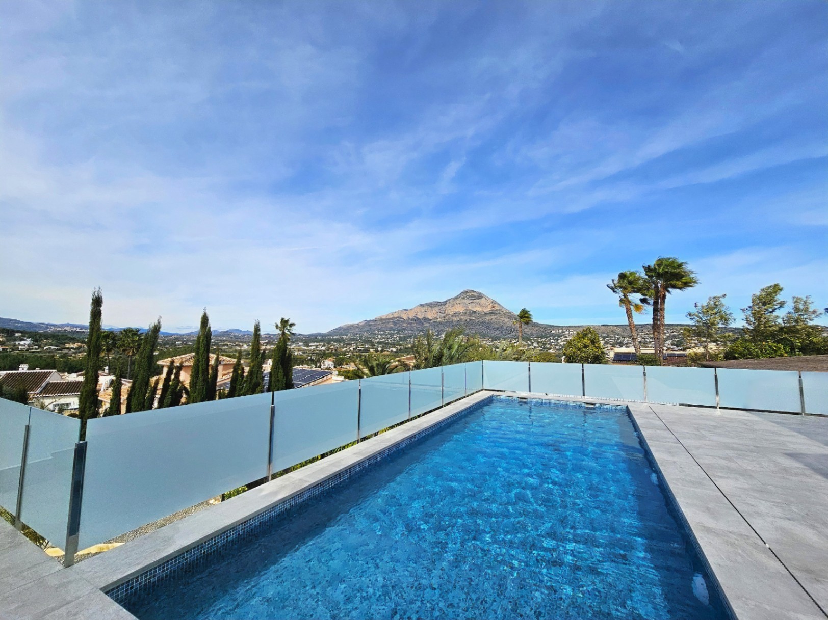 Blick auf den blau gefliesten Pool mit Glasgeländer und Blick auf den Montgó.