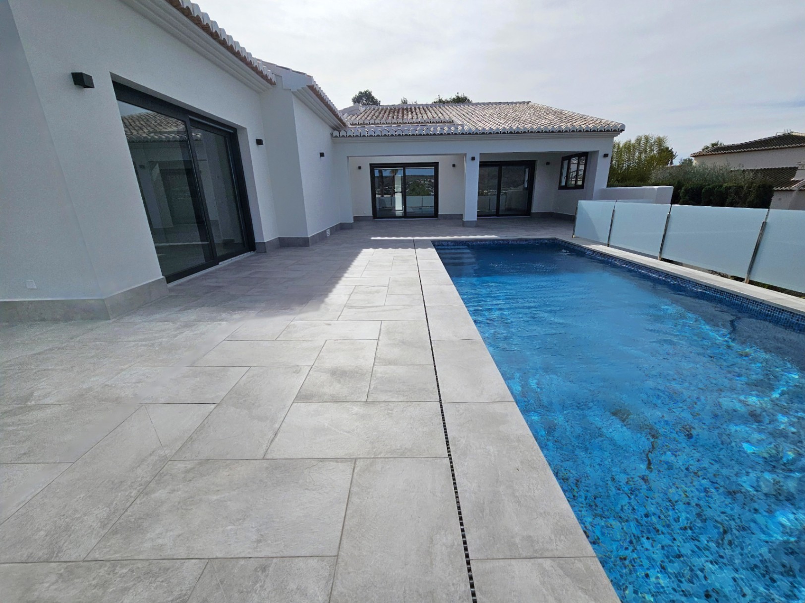 Blick auf die gepflasterte Terrasse mit Pool und Glasgeländer.