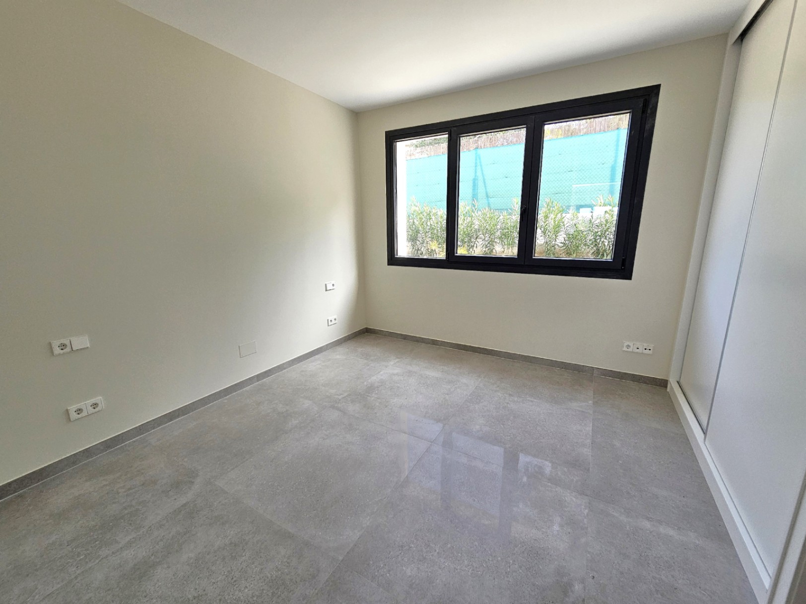 Helles Schlafzimmer mit Feinsteinzeugboden und dreifach verglastem Fenster mit schwarzem Rahmen.