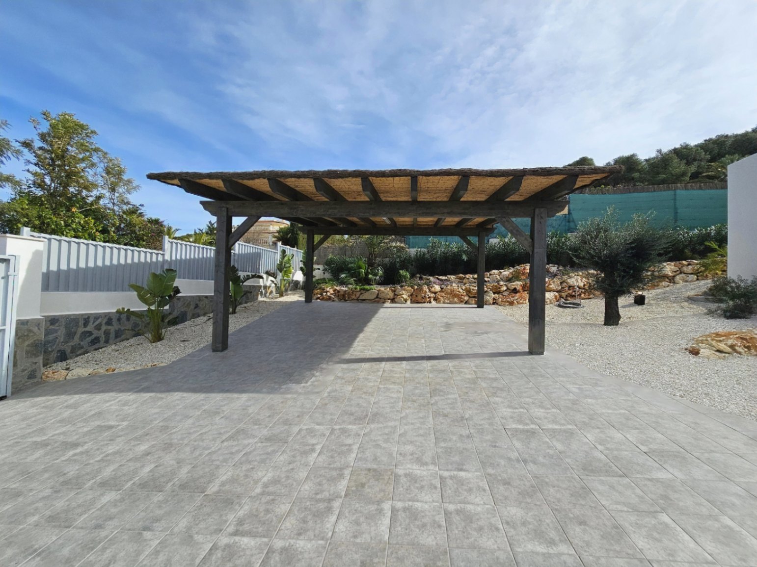 Holzpergola mit Strohdach über grau gefliestem Boden im Parkbereich.