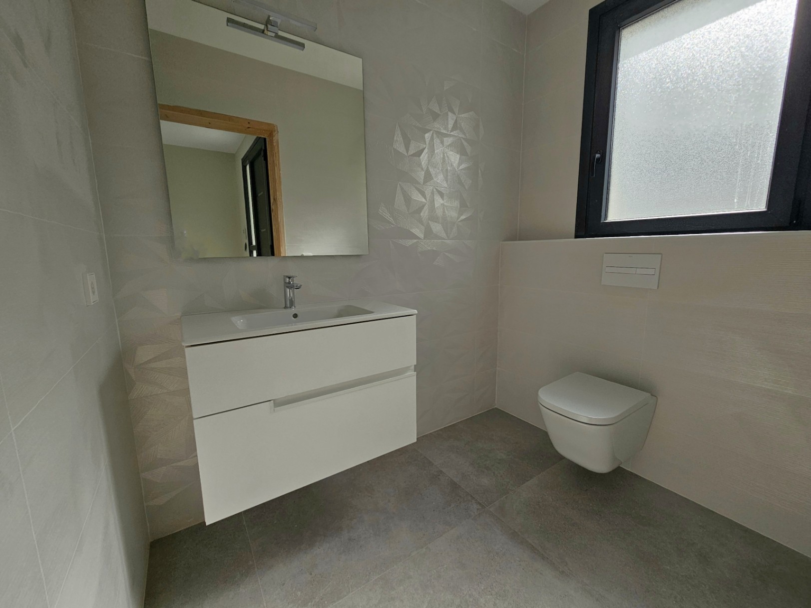 Modernes Badezimmerdetail mit weißem Hängewaschtisch, Toilette und geometrischen Fliesen.