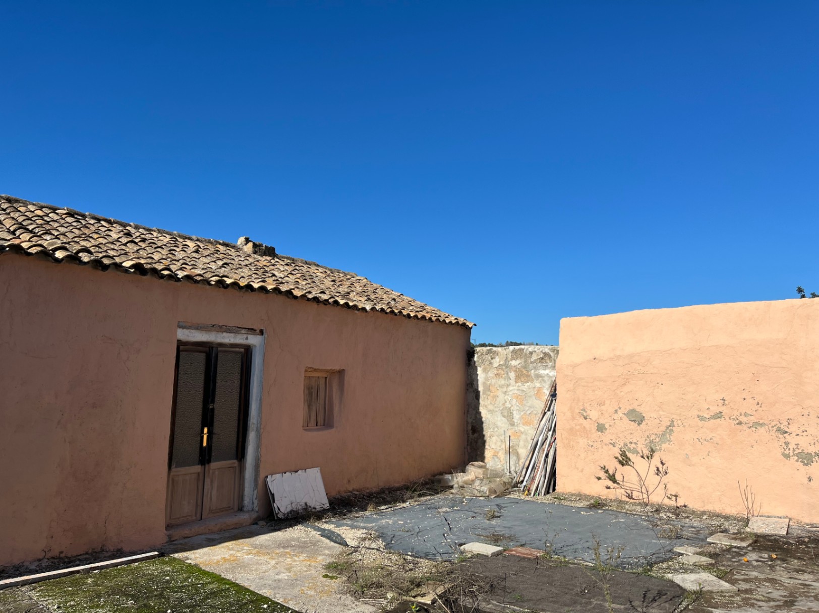 Außenansicht einer traditionellen Finca mit terrakottafarbener Fassade, Tonziegeldach und Holztür, ideal für ein umfassendes Renovierungsprojekt.