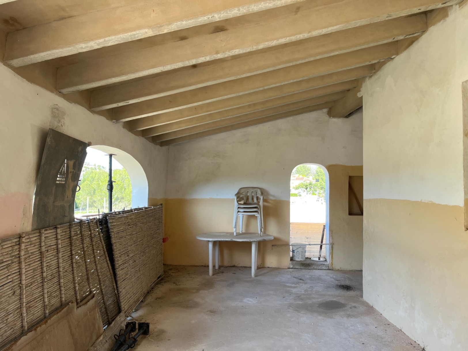 Innenraum mit Dachschräge, sichtbaren Holzbalken und Rundbogenöffnungen. Der Raum befindet sich im Originalzustand und bietet Potenzial für eine Renovierung.